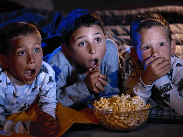 3 kids eating popcorn and gasping at spooky movies