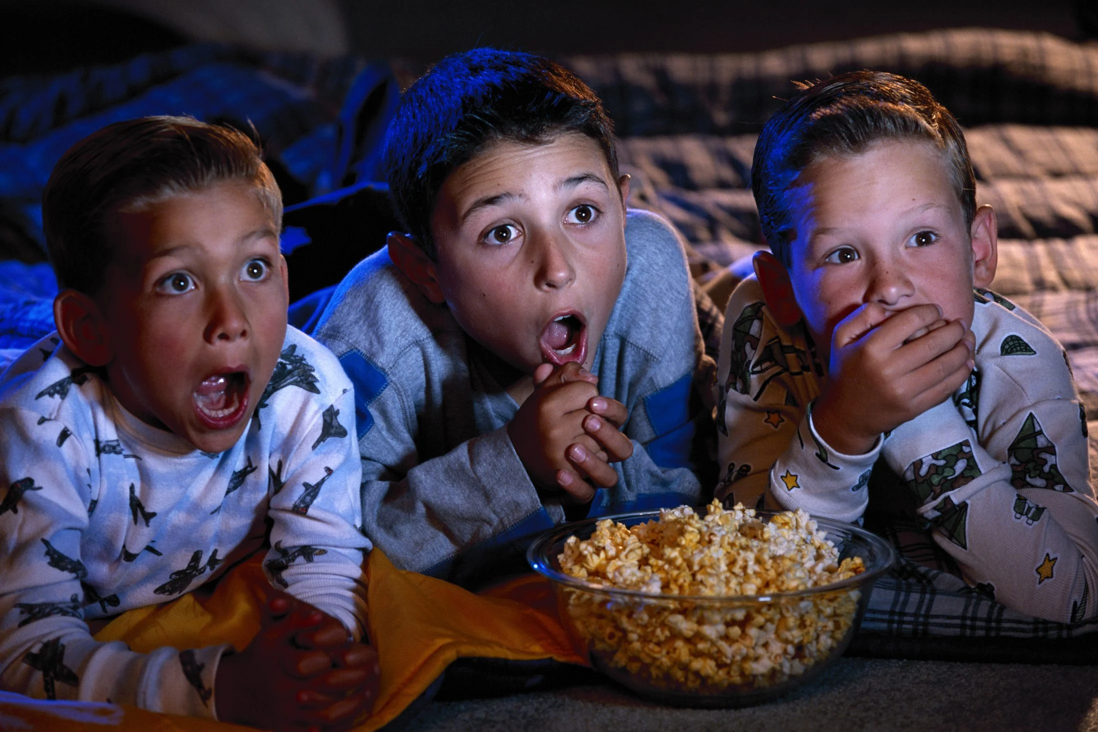 3 kids eating popcorn and gasping at spooky movies