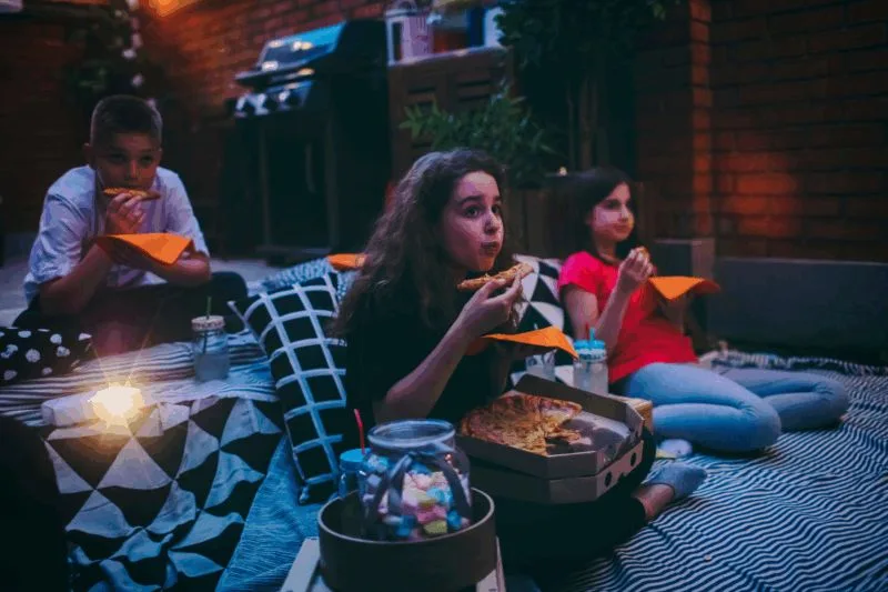 children eating pizza outdoors watching movie